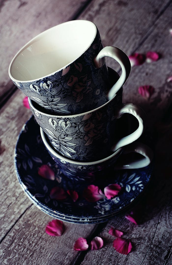 Vintage floral teacups stacked with rose petals on a rustic wooden table. Elegant and timeless.