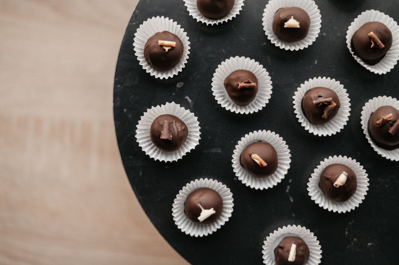 A delicious assortment of chocolate pralines presented in white papers on a black plate, viewed from above.